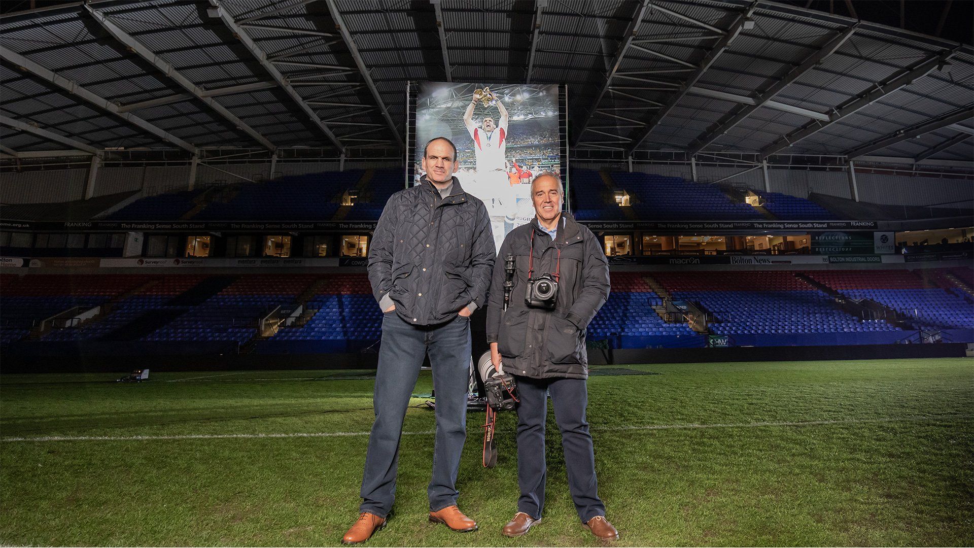 Sports photographer Dave Rogers stands next to rugby player Martin Johnson on the pitch.
